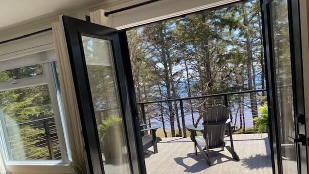 Una puerta corrediza de vidrio moderna que da a una terraza exterior con vistas a un bosque y una mesa con sillas.
