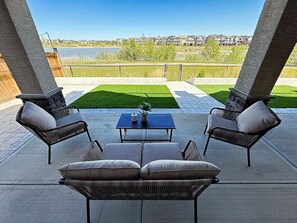 An outdoor patio with a blue table and four wicker chairs, overlooking a body of water and a residential area. - Mahogany Lakefront 2BR Walkout | Trails & Privacy (Calgary)