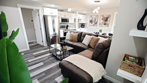 A modern living room with a brown leather sofa, a glass coffee table, and a white throw blanket. - Mahogany Lakefront 2BR Walkout | Trails & Privacy (Calgary)