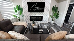 A modern living room with a black leather sofa, a glass coffee table, and a fireplace. - Mahogany Lakefront 2BR Walkout | Trails & Privacy (Calgary)