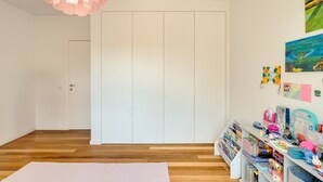 Une pièce avec un plancher en bois, une porte blanche, une armoire blanche et une étagère remplie de livres et de jouets.