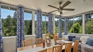 A sunroom with a dining table, chairs, and a ceiling fan. - Redwood Retreat  Sauna, Plunge, Jacuzzi & Views (Camp Meeker)