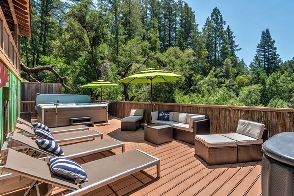 Une terrasse avec des chaises longues, un jacuzzi et des parasols verts.