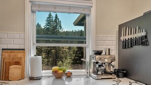A kitchen with a marble countertop, a coffee machine, a bowl of fruit, and a window with a view of trees. - Redwood Retreat  Sauna, Plunge, Jacuzzi & Views (Camp Meeker)
