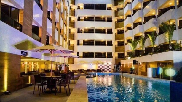 A hotel interior with a swimming pool, multiple floors, and outdoor seating areas. - Nomar VI (Joao Pessoa)