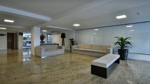 A spacious lobby with a marble floor, a reception desk, a sofa, a bench, and potted plants. - Nomar VI (Joao Pessoa)