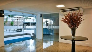 A modern lobby with a glass partition, a round table with a vase, and a blue carpet. - Nomar VI (Joao Pessoa)