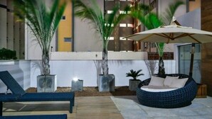 An outdoor lounge area with lounge chairs, a round seating area, and potted plants. - Nomar VI (Joao Pessoa)