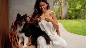 Una persona sentada en una silla de mimbre al aire libre, con un perro, sosteniendo una taza.