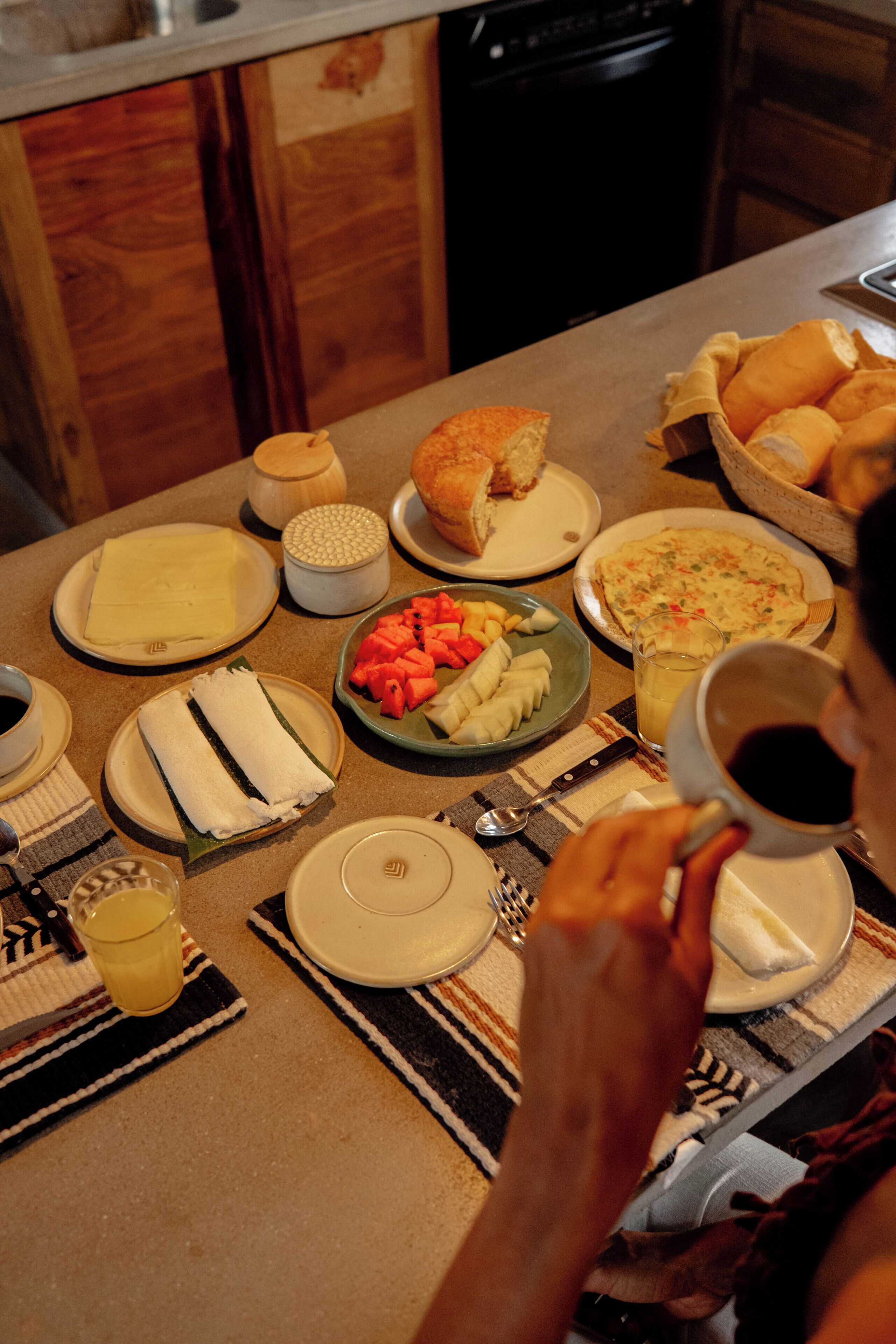 A breakfast table with plates of food, a cup of coffee, and a bottle of juice.