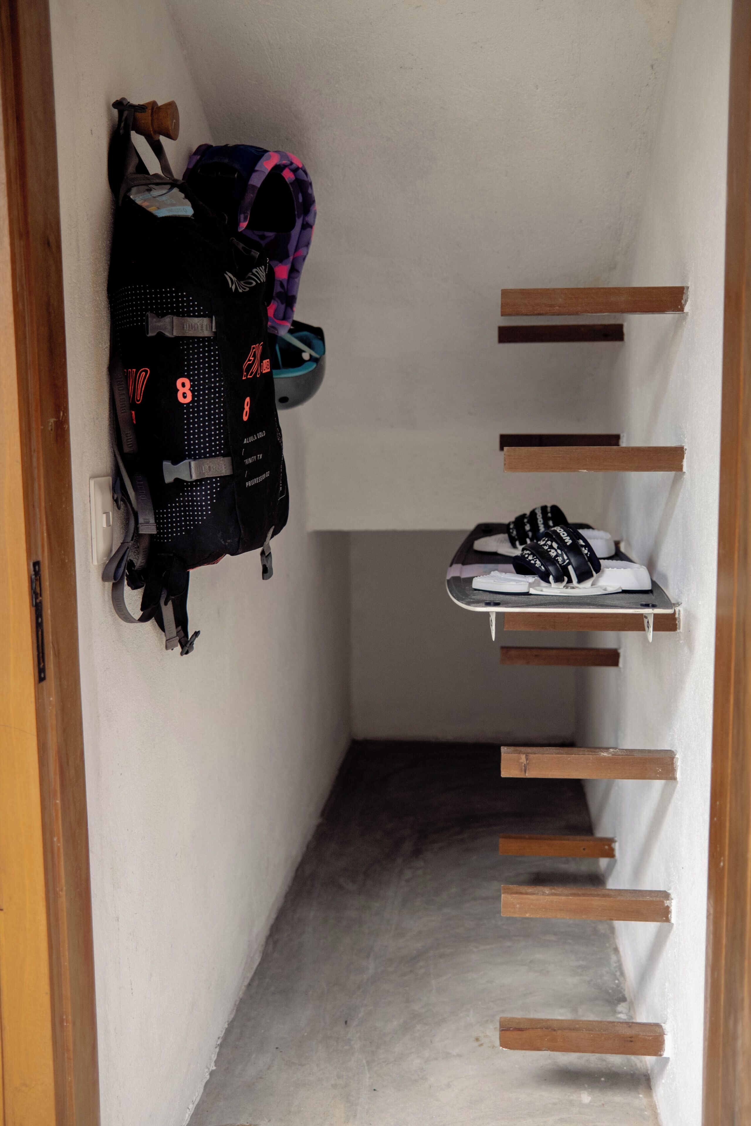 A narrow hallway with a wooden door frame, a black backpack, and a pair of white sneakers on a shelf.