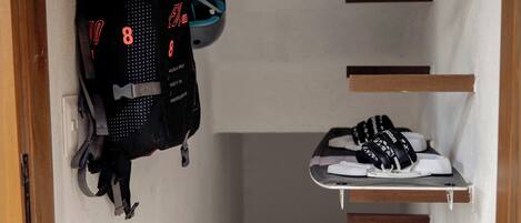 A narrow hallway with a wooden door frame, a black backpack, and a pair of white sneakers on a shelf.