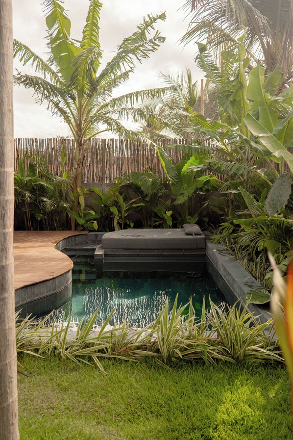 A pool area with a wooden deck, surrounded by lush tropical plants and a bamboo fence.