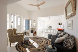 A spacious living room with a large round rug, a ceiling fan, and a black sofa with patterned cushions.