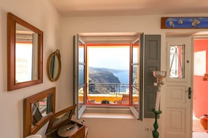 A room with a balcony overlooking a coastal landscape, a door with a decorative handle, and a mirror on the wall.