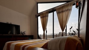 A modern hotel room with a large bed, a flat-screen TV, and a view of the outdoors.