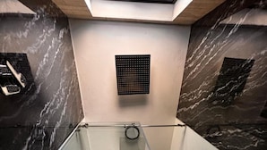 A narrow, glass-walled bathroom with a marble wall, a towel rack, and a toilet.