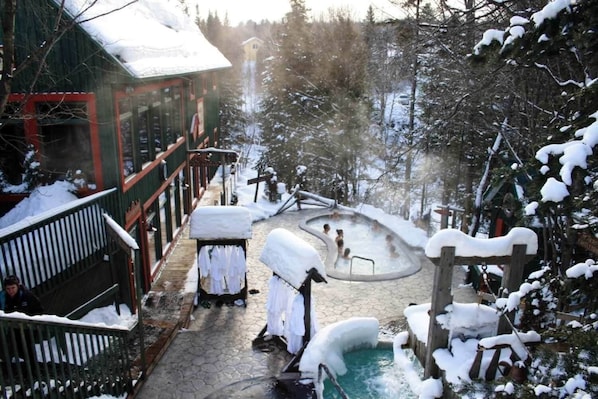 A snow-covered outdoor area with a hot tub, wooden deck, and a building with a red frame.