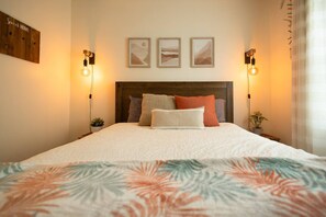 A neatly made bed with a floral-patterned bedspread, a wooden headboard, and three framed artworks above it. - The Peaks and the Water (Magog)