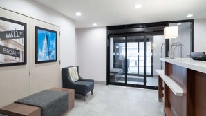 Un área de recepción moderna con mostrador, zona de estar con sofá y sillón, y vistas a un espacio exterior a través de un ventanal.