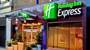 A Holiday Inn Express building with a prominent green logo, a glass entrance, and a bench outside. - Close to Times Square + Free Breakfast & Wi-Fi (New York)