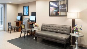 A hotel lobby with a sofa, two chairs, a desk with a computer, a lamp, and a framed picture of Wall Street. - Steps from Wall Street | Free Breakfast. Gym (New York)