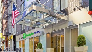 A Holiday Inn Express hotel with a glass entrance canopy, large windows, and potted plants. - Steps from Wall Street | Free Breakfast. Gym (New York)