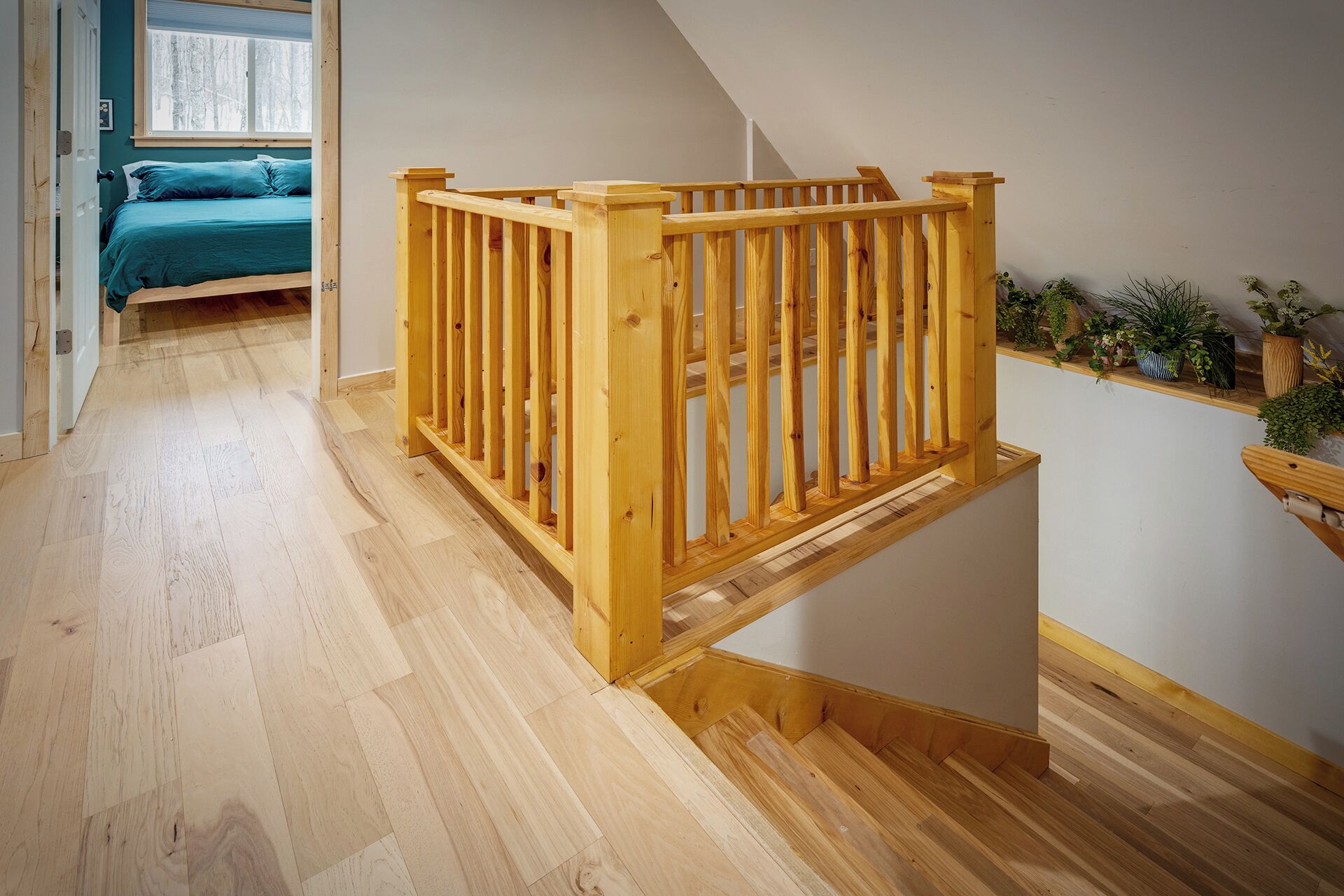 A wooden staircase with a railing leading to a bedroom with a blue bed.