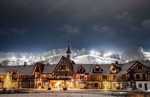 Un bâtiment de style européen traditionnel, doté de plusieurs toits à pignons, d’une tour imposante et, en arrière-plan, d’un paysage enneigé.