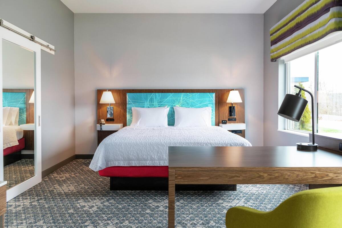 Una habitación de hotel con una cama, mesitas de noche, un escritorio, una silla y una ventana con cortinas.