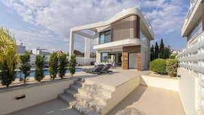 A modern two-story house with a pool, outdoor seating, and a staircase leading to the entrance.