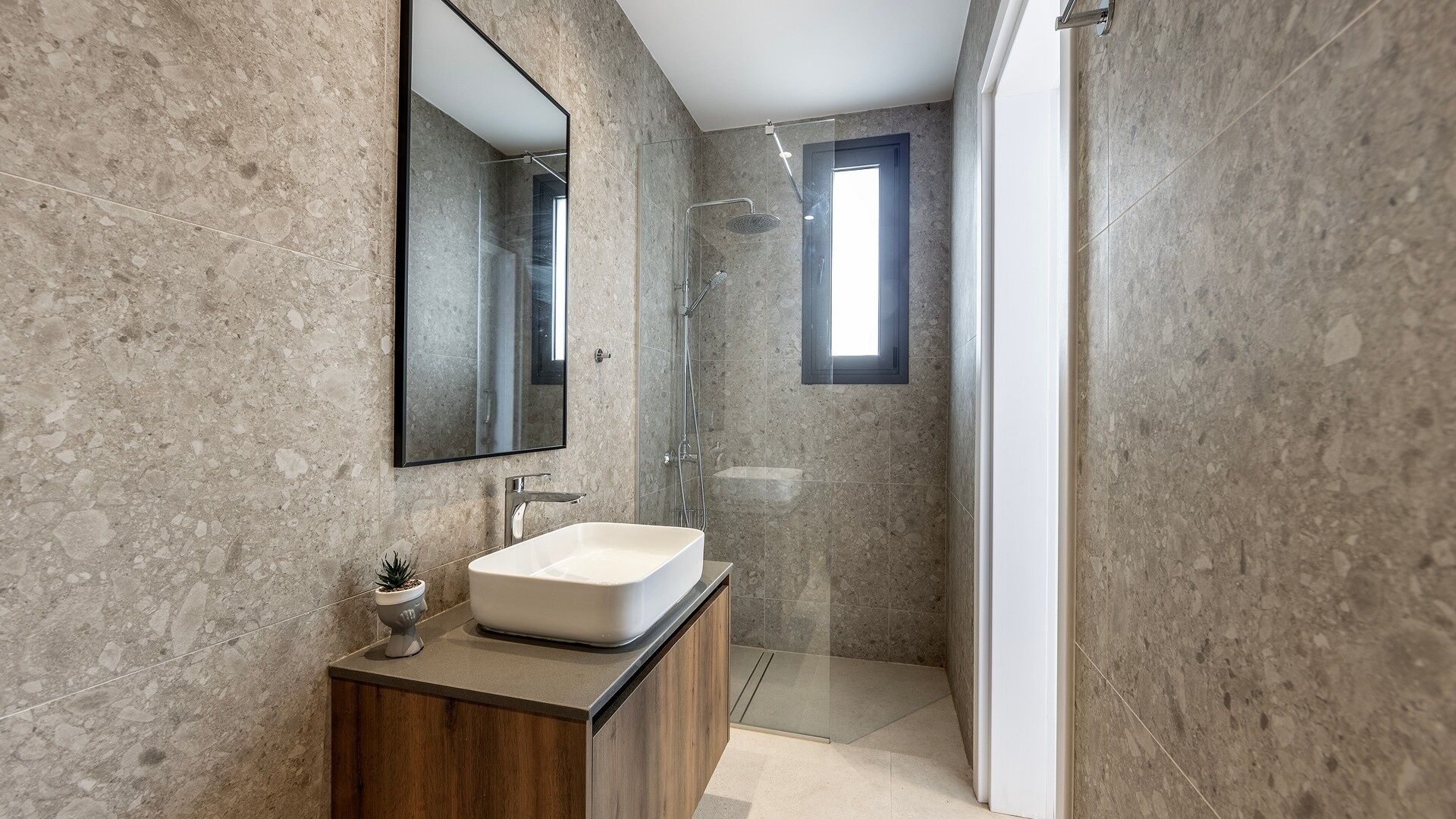 Un baño moderno con un espejo grande, un lavamanos independiente y una ducha con mampara de vidrio.