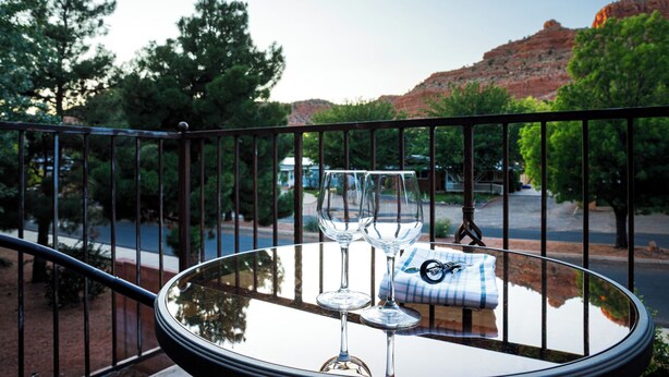 Una mesa de vidrio con dos copas de vino y una servilleta en un balcón con vistas a un paisaje pintoresco con árboles y una colina.