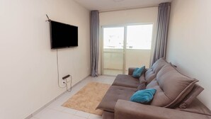 Ein Wohnzimmer mit einer Couch, einem Flachbildfernseher, einer Steckdose und einer Glastür zum Balkon.