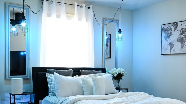 A bedroom with a bed, a ceiling fan, a nightstand, a lamp, and a window with curtains.