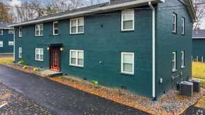 A two-story building with a dark green exterior, a red door, and a small front porch.