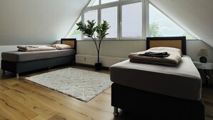 Une chambre avec un plafond en pente, une grande fenêtre, un lit, un banc et une plante en pot.