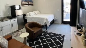 Habitación de hotel compacta con kitchenette, una cama, zona de estar con sofá y sillón, una mesita y televisor.