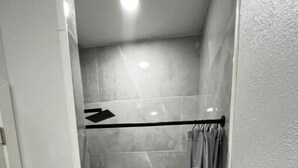Un espacio de ducha pequeño y cerrado con puerta de vidrio, un perchero y una cortina de ducha.