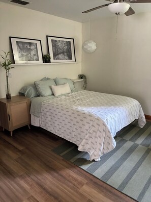 A bedroom with a bed, a nightstand, a wall-mounted shelf with plants, and a ceiling fan.