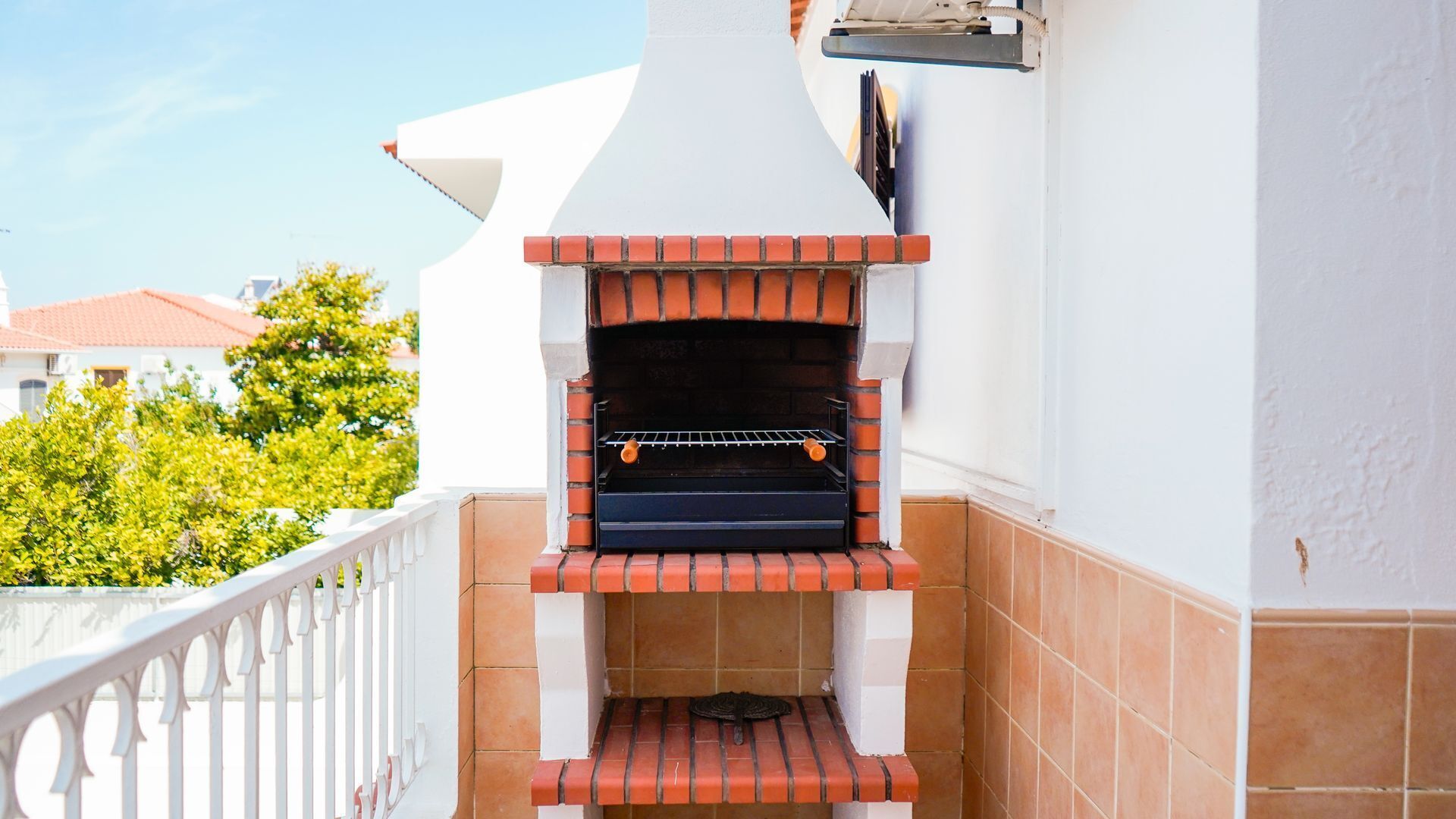 A brick-built outdoor oven attached to a white wall, with a metal rack for hanging items.