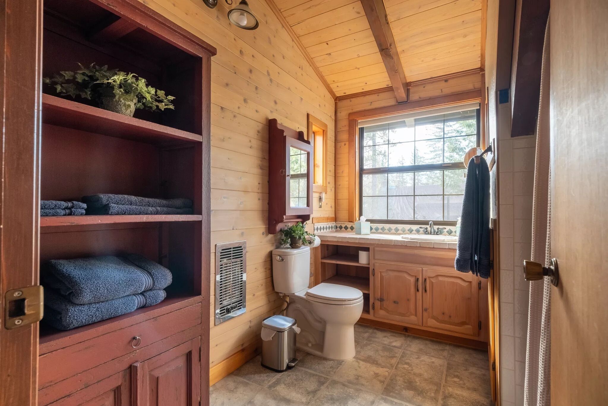Een houten badkamer in een vakantiehuisje, met een toilet, wastafel en planken met handdoeken.