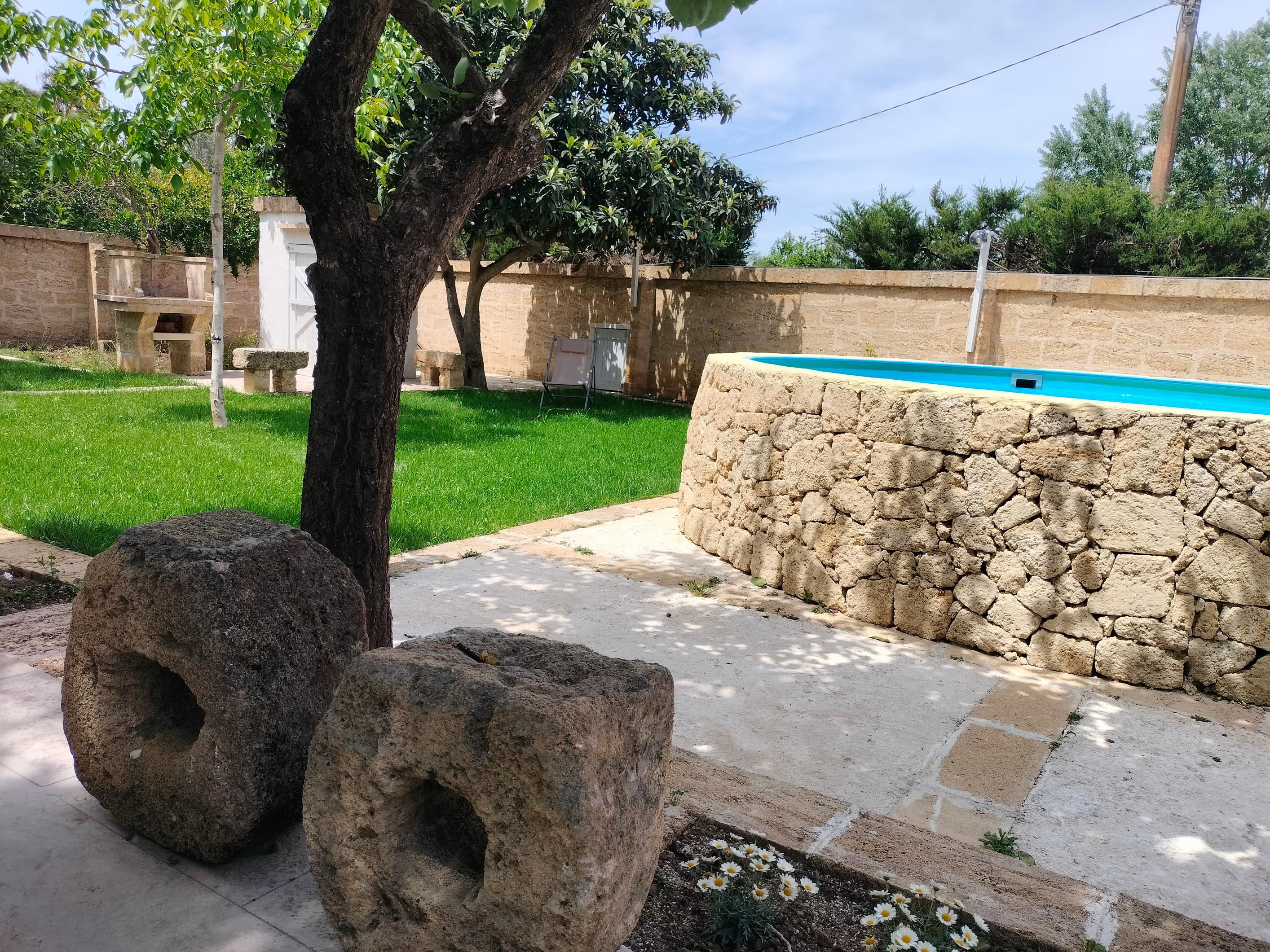 Un giardino con un muro in pietra, un albero e una piscina.