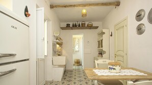 Una cocina estrecha con suelo de baldosas, una mesa de madera con un mantelillo, y un refrigerador con la etiqueta 