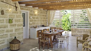 Una cocina rústica con una mesa y sillas de madera, una pared de piedra y vistas a la vegetación a través de una ventana.