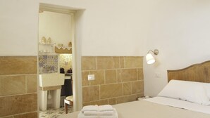 Habitación de hotel con cama, mesita de noche, lámpara de noche, espejo y baño visible a través de una puerta abierta.