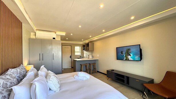 A modern hotel room with a large bed, a desk area, and a TV. - Newly renovated, charming studio in central Jeffreys Bay with AC, WiFi, parking (Jeffreys Bay)