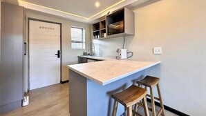A modern kitchen with a central island, wooden stools, and built-in shelves. - Newly renovated, charming studio in central Jeffreys Bay with AC, WiFi, parking (Jeffreys Bay)