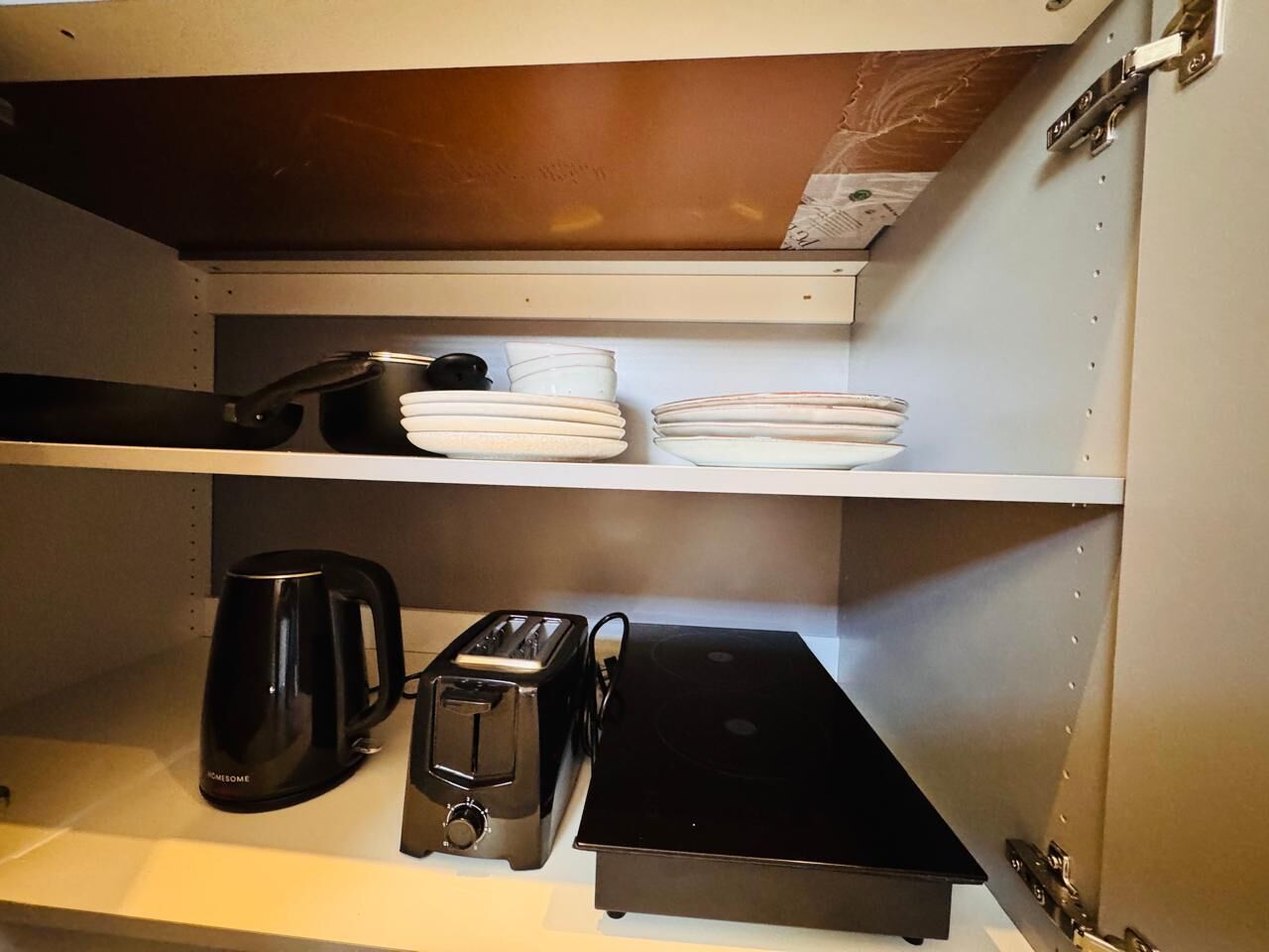 Een keuken met een koffiezetapparaat, broodrooster en gestapelde borden op de planken.