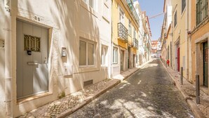 Una estrecha calle adoquinada flanqueada por edificios de arquitectura tradicional, una puerta con dispositivo de seguridad y un pequeño canal de desagüe.